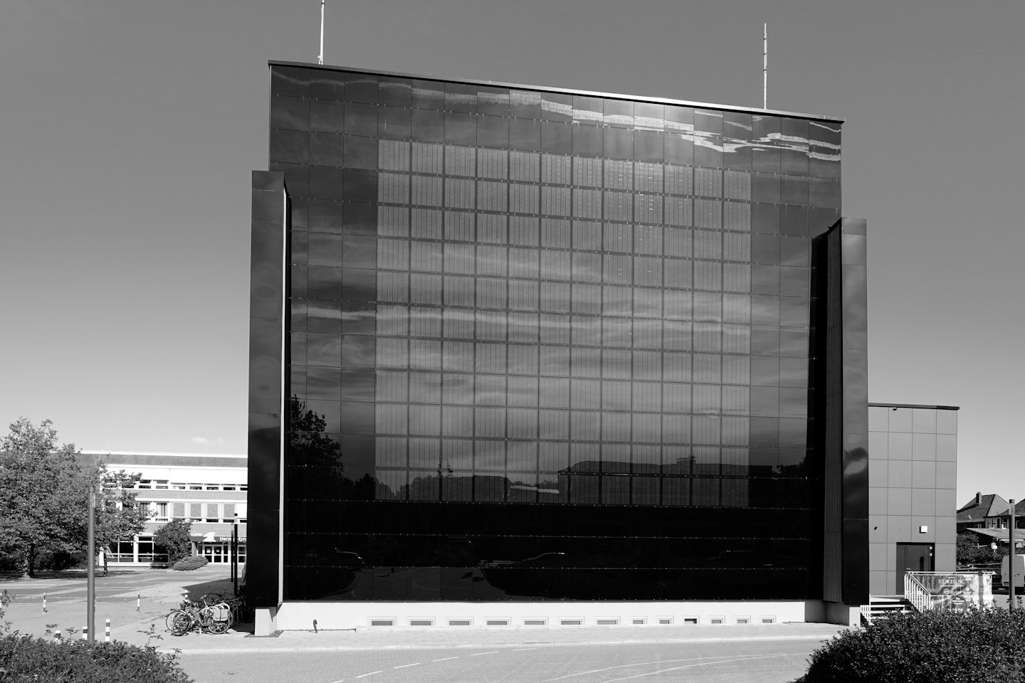 Moderno edificio per uffici con facciata riflettente di pannelli solari e biciclette parcheggiate.